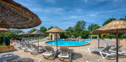 Piscina all'aperto con lettini e ombrelloni di paglia al Camping Le Clou, Nouvelle-Aquitaine, Francia.