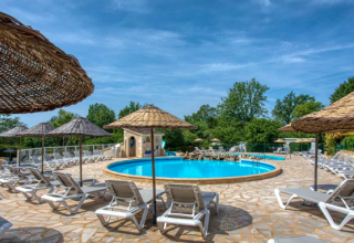 Außenpool mit Liegestühlen und Strohdächern im Ferienpark Camping Le Clou, Nouvelle-Aquitaine, Frankreich.