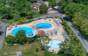 Aerial view of Camping Le Clou in Nouvelle-Aquitaine, France, featuring pools, sun loungers, a playground and lush greenery.