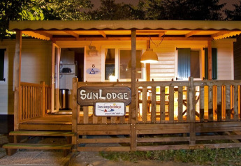 Night view of a warmly lit wooden lodge with a porch, sign reading SunLodge, and cozy atmosphere.