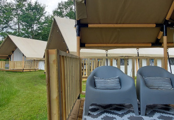 To grå stole med puder på en terrasse foran en safaritelte ved Beloofde Land i Holland, omgivet af natur.