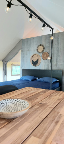 Intérieur d'une tente safari à Beloofde Land avec lit double, table en bois, décoration murale et guirlandes.
