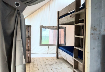 Interior de una tienda safari en Beloofde Land, Países Bajos, con literas y suelo de madera claro.