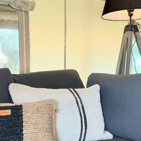 Innenaufnahme eines Safarizeltes im Beloofde Land, Niederlande, mit blauem Sofa, Kissen und Lampe.