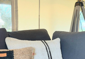 Interior view of Safaritent at Beloofde Land in the Netherlands, featuring blue sofa, cushions, and lamp.