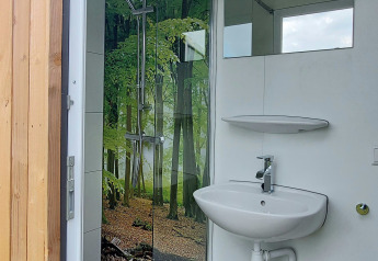 Badezimmer im Safarizelt am Beloofde Land in den Niederlanden, mit Waldfotomotiv in der Dusche.