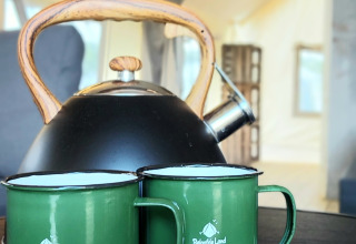 Black teapot with wooden handle and two green mugs on a table in a safari tent at Beloofde Land, Netherlands.