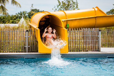 En pige nyder en tur på en gul vandrutsjebane, der ender i en pool på et glamping-ophold.