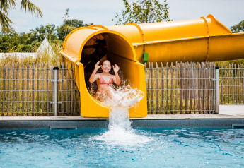 Una ragazza si tuffa in piscina dallo scivolo giallo in una struttura glamping in una giornata di sole.