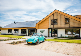 Une voiture rétro bleue stationnée devant un hébergement glamping moderne avec des panneaux solaires.