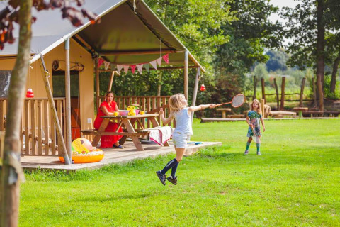 Børn leger badminton foran et safaritelts terrasse på Beloofde Land i Holland, en kvinde ser på.