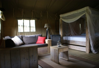Interior of Safaritent at Beloofde Land in the Netherlands, featuring a wooden bed, sofa and rustic charm.