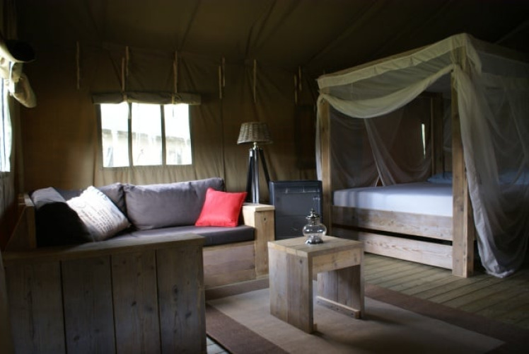 Interieur van Safaritent op Beloofde Land in Nederland, met houten bed, bank en sfeervolle inrichting.