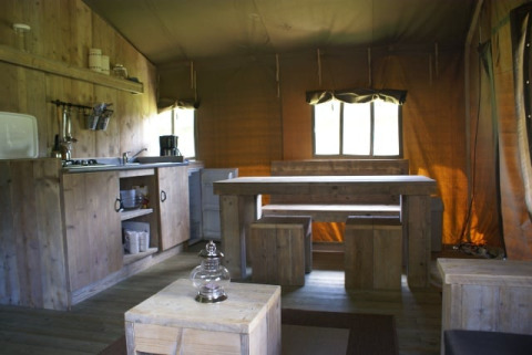 Interior de la tienda safari Safaritent en Beloofde Land, Países Bajos, con muebles de madera y cocina.