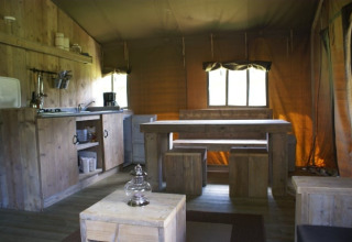 Interior de la tienda safari Safaritent en Beloofde Land, Países Bajos, con muebles de madera y cocina.