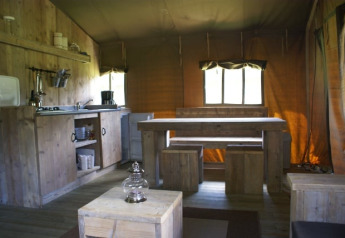 Interior de la tienda safari Safaritent en Beloofde Land, Países Bajos, con muebles de madera y cocina.