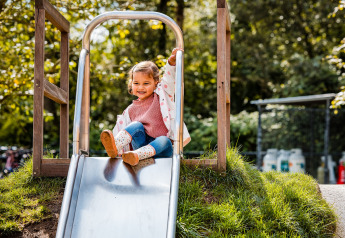 Niña deslizándose en un tobogán metálico en Safaritent del Beloofde Land, Países Bajos, al aire libre.