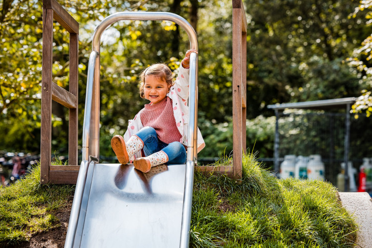 Niña deslizándose en un tobogán metálico en Safaritent del Beloofde Land, Países Bajos, al aire libre.
