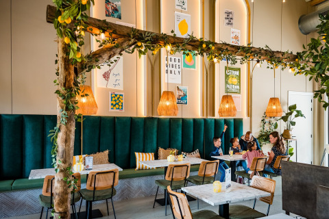Een modern glampingrestaurant met groene banken, houten decoratie en een gezin dat samen aan tafel zit.