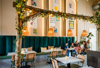 Un restaurant de glamping moderne avec banquettes vertes, déco bois et famille partageant un repas ensemble.