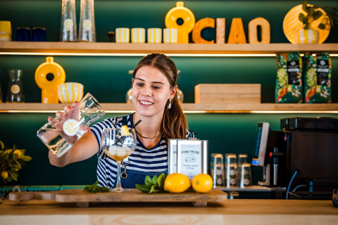 Una camarera sonriente sirve una bebida de limón en una elegante barra de glamping decorada modernamente.
