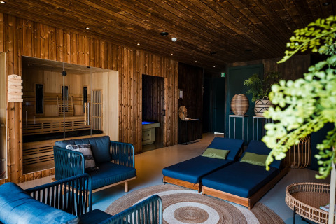Interior de tienda safari con paredes de madera, zona lounge, sauna, decoración moderna y plantas verdes.