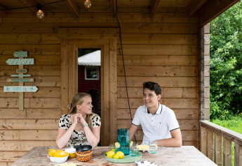 Zwei junge Leute sitzen an einem Holztisch in einem Safarizelt namens Lego huisje in Beloofde Land.