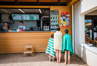 Three children in towels stand in front of a snack bar at a safari tent camp, deciding on ice cream.