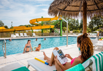 Familia disfruta en la piscina con tobogán y sombrilla de paja en un camping de tiendas safari.