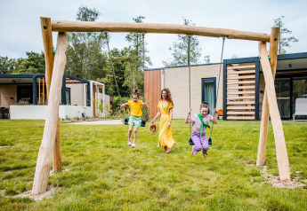 Trois enfants jouent et se balancent devant une tente safari avec herbe verte et hébergements modernes.