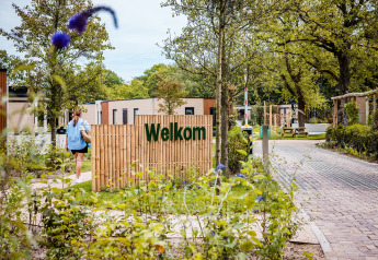 Toegang tot een safaritentenpark met welkom-bord, tuin en een persoon die naar de verblijven wandelt.