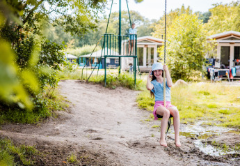 Ragazza sull’altalena in un glamping, con bungalow sullo sfondo, atmosfera di vacanza estiva all’aperto.