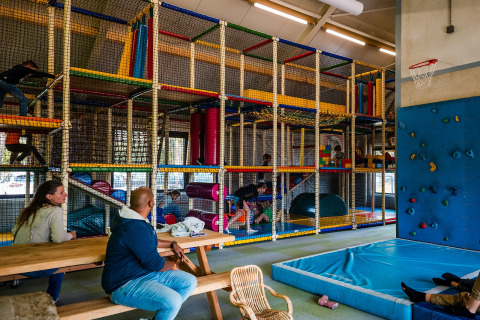 Indoor speeltuin met klimstructuur, klimmuur en volwassenen aan tafels bij Beloofde Land, Nederland.