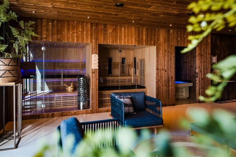 Moderne glamping-accommodatie met houten wanden, glazen sauna’s, comfortabele zitplaatsen en planten.