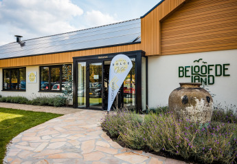 Entrada al restaurante Beloofde Land en los Países Bajos con carteles de bienvenida y gran tinaja de barro.
