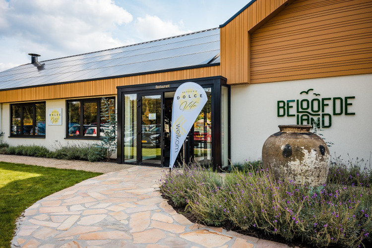 Eingang des Restaurants Beloofde Land mit Werbeflaggen, Lavendelbeeten und einem großen Tonkrug.