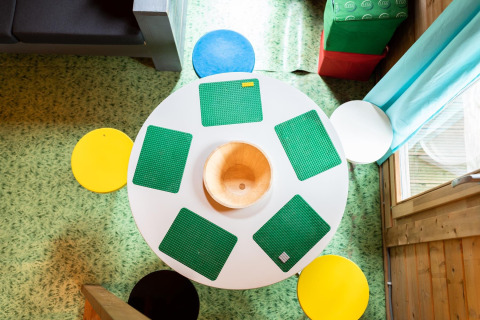 Top view of a round table with green LEGO mats and colorful stools in a safari tent at Beloofde Land, Netherlands.
