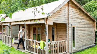 Foto di una tenda safari in legno con veranda e prato verde, persone che si rilassano all'esterno.