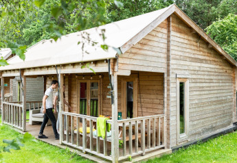 Foto eines Safari-Zelthauses aus Holz mit Veranda im Grünen, während Menschen davor entspannen.