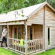 Photo of a wooden safari tent cabin with porch in a green setting, people relaxing on the terrace outside.