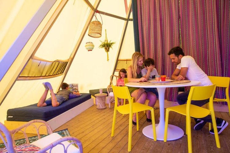 Gezin geniet in Jippi Tippi tipi-tent op Beloofde Land, Nederland, kinderen lezen en spelen samen.