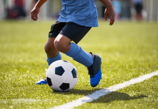A child in blue soccer gear dribbles a black and white soccer ball on a grassy field near the sideline.