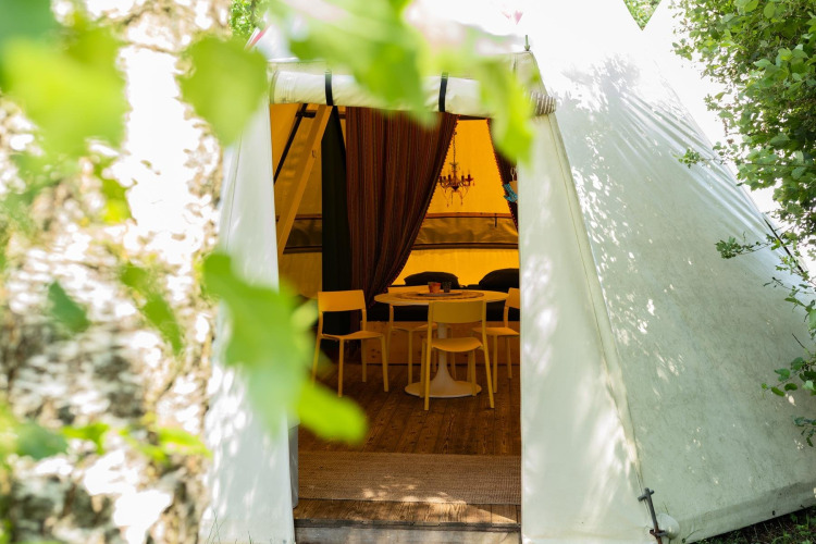 Ingang van de Jippi Tippi tent bij Beloofde Land in Nederland met tafel en stoelen zichtbaar binnenin.