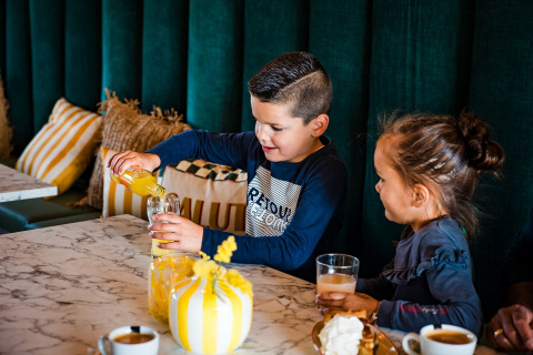 Twee kinderen drinken sap aan een marmeren tafel in een tipi-tent bij Beloofde Land, Nederland.