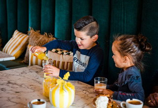 Twee kinderen drinken sap aan een marmeren tafel in een tipi-tent bij Beloofde Land, Nederland.