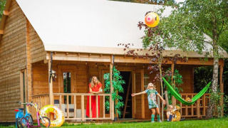 Famille profitant devant leur tente safari Jungle huisje, enfants jouant avec un ballon sur la pelouse verte.