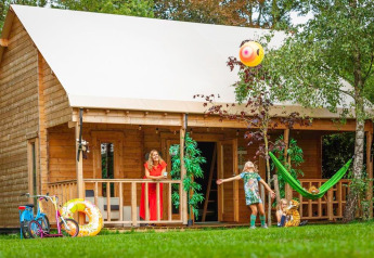 Familia disfrutando afuera de su tienda safari Jungle huisje, niños jugando con una pelota en el césped.