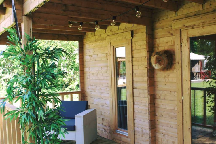 Houten veranda met bank, planten en lampjes bij Jungle huisje safaritent in Beloofde Land, Nederland.