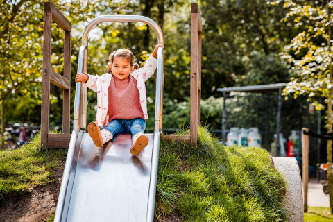 A young child enjoys sliding down a metal slide at Zweedse Huisjes, Beloofde Land, Netherlands playground.