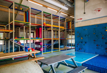 Buntes Indoor-Spielplatz mit Kletterstruktur, Boulderwand, Sitzbänken und weichen Matten in einer Lodge.